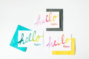 Three coloured envelopes, blue, yellow and dark grey with postcards on top saying Hello there to illustrate email marketing